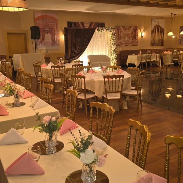 Elegant Indian restaurant interior with tables set for an event, featuring floral centerpieces and golden chairs.