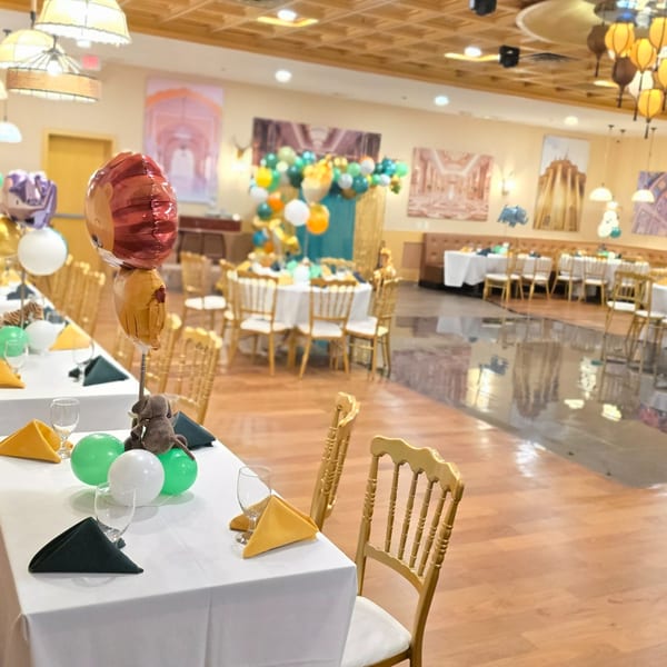 A restaurant dining room set up for a party with white tablecloths, gold chairs, and animal balloons.