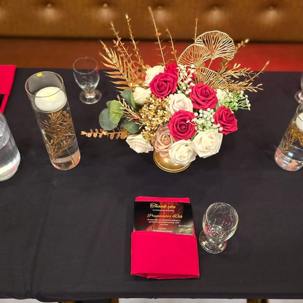 A black table set with a floral centerpiece, candles, glasses, and a "Thank You" card.