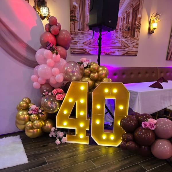 A large, illuminated "40" sign stands amidst pink, gold, and maroon balloons with floral accents.
