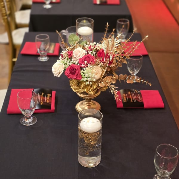 Elegant table setting with red and cream floral centerpiece, golden accents, and floating candles.