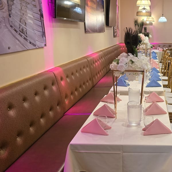 Long dining table with pink and blue napkins, floral centerpieces, and brown booth seating.