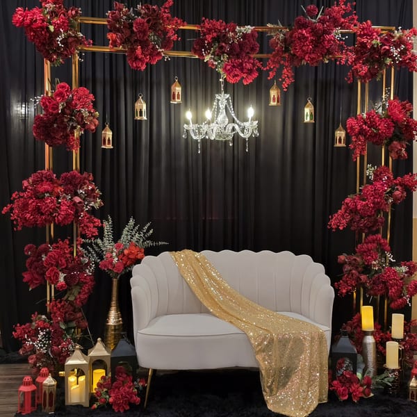 Elegant Indian-themed decor with a white sofa, red flowers, golden lanterns, and a crystal chandelier.