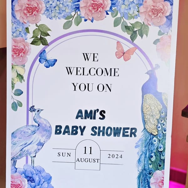 Baby shower welcome sign with peacocks, butterflies, and pink and blue flowers.