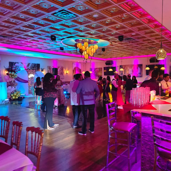 Guests mingle in a vibrant Indian restaurant dining room with purple and blue lighting.