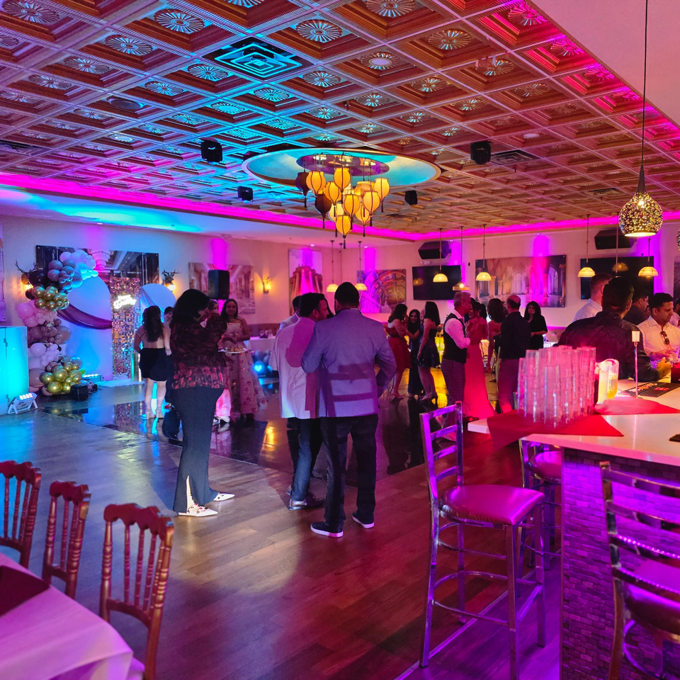 Guests mingle in a vibrant Indian restaurant dining room with purple and blue lighting.