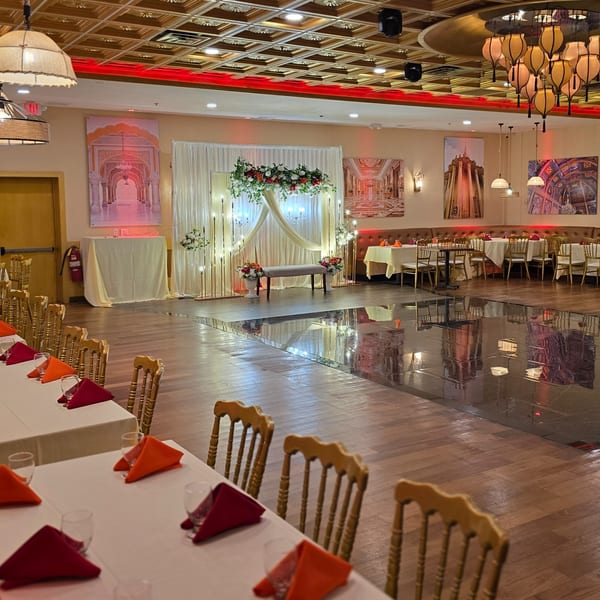 An empty Indian restaurant dining room with a decorated stage, tables set with red and orange napkins.