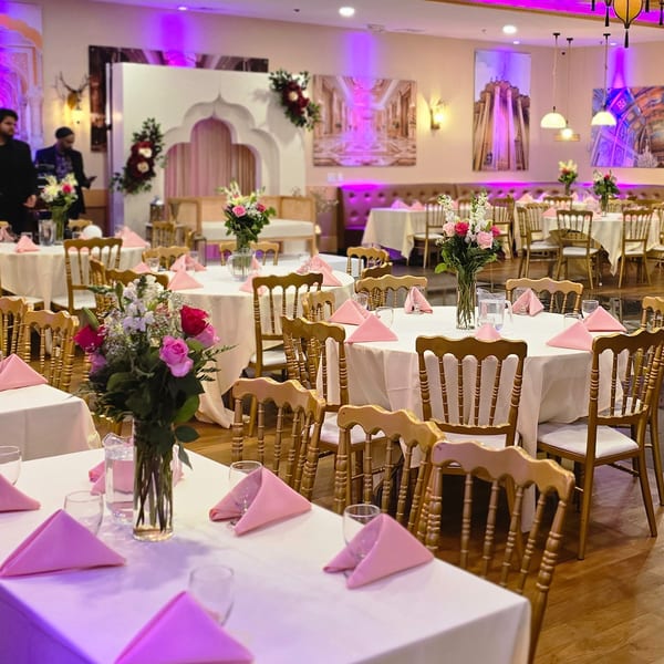 Elegant Indian restaurant dining room with white tablecloths, pink napkins, floral centerpieces, and purple lighting.
