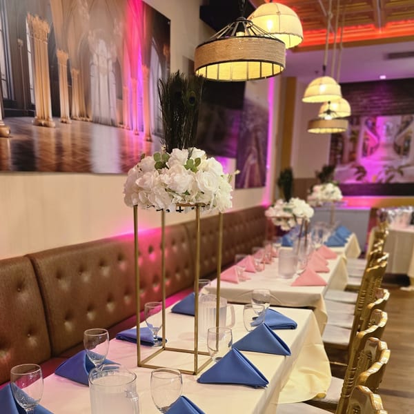 Long dining tables set with blue and pink napkins, white floral centerpieces, and ornate gold chairs.