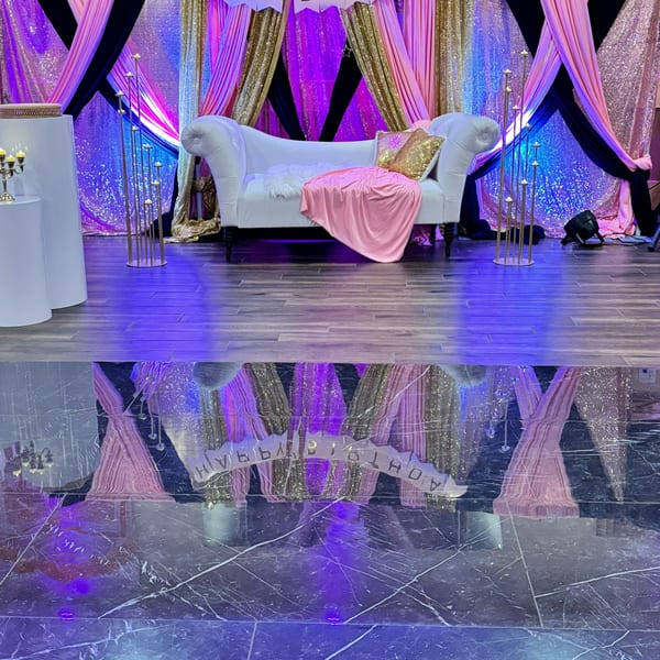 Elegant stage with a white sofa, pink and gold drapes, and candle stands, reflecting on a shiny floor.