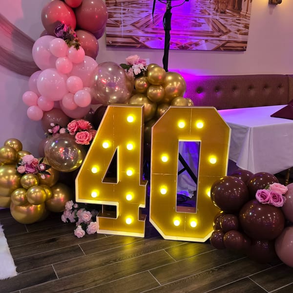 Large illuminated "40" sign surrounded by pink, gold, and maroon balloons with flowers at Spice Culture.