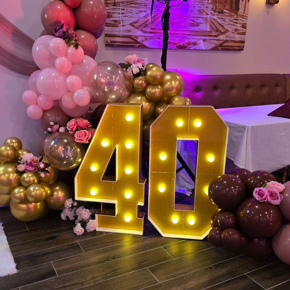 Large illuminated "40" sign surrounded by pink, gold, and maroon balloons with flowers at Spice Culture.