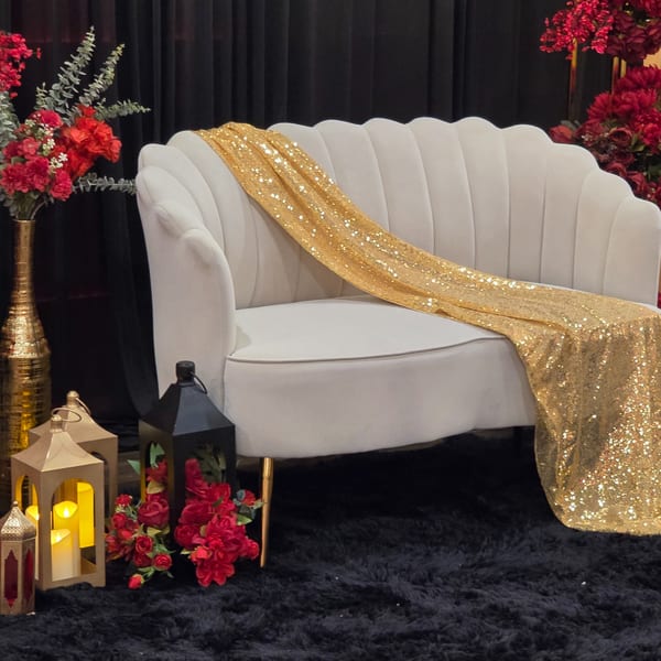 A plush white sofa draped with a gold sequin fabric, surrounded by red flowers and lanterns.