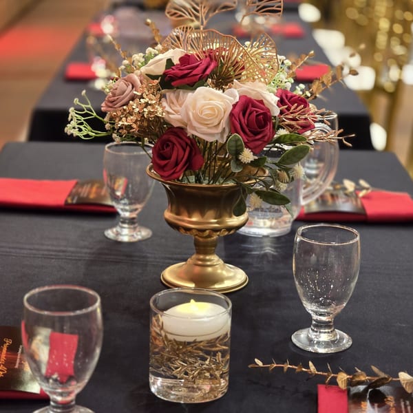 A formal table setting with a gold vase holding red and white roses, glasses, and a candle.