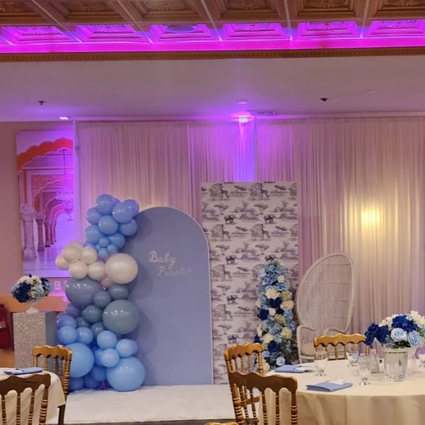 A baby shower setup with blue and white balloons, floral arrangements, and dining tables.