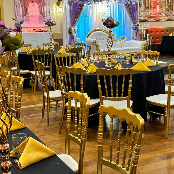 Elegant Indian banquet hall with black tables, gold chairs, yellow napkins, and a white and gold sofa.