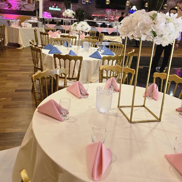Elegant dining room at Spice Culture with tables set with pink and blue napkins, gold chairs, and floral centerpieces.