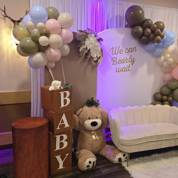 Baby shower decor with balloons, a large teddy bear, and a sign reading "We can Bearly wait".