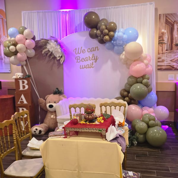 A baby shower setup with balloons, a teddy bear, and a table with traditional Indian decorations.