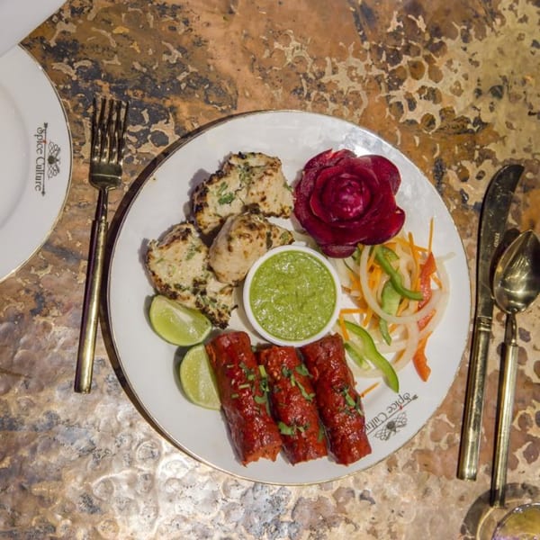 A Spice Culture plate with chicken tikka, seekh kebab, green chutney, lime, and salad.
