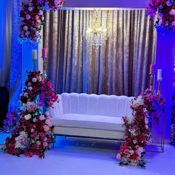 Elegant white sofa with floral arrangements and candelabras, set against a shimmering curtain and chandelier.