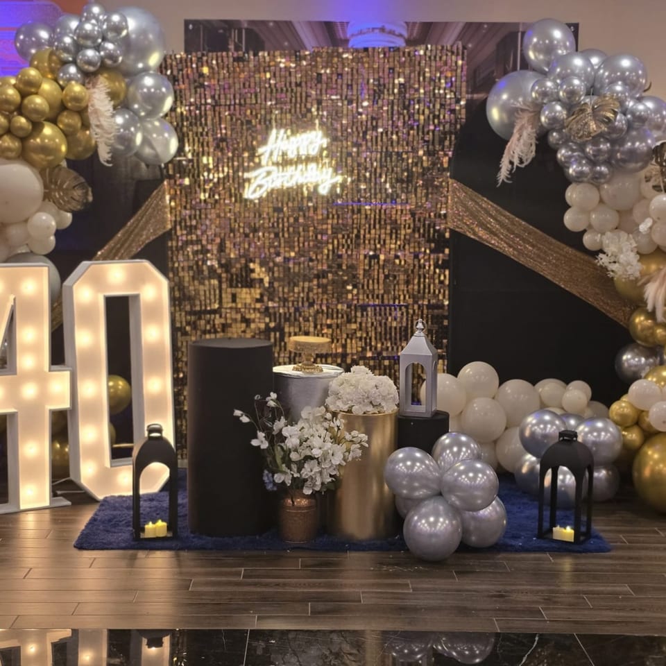 A festive birthday display with gold and silver balloons, a 'Happy Birthday' neon sign, and illuminated '40' numbers.