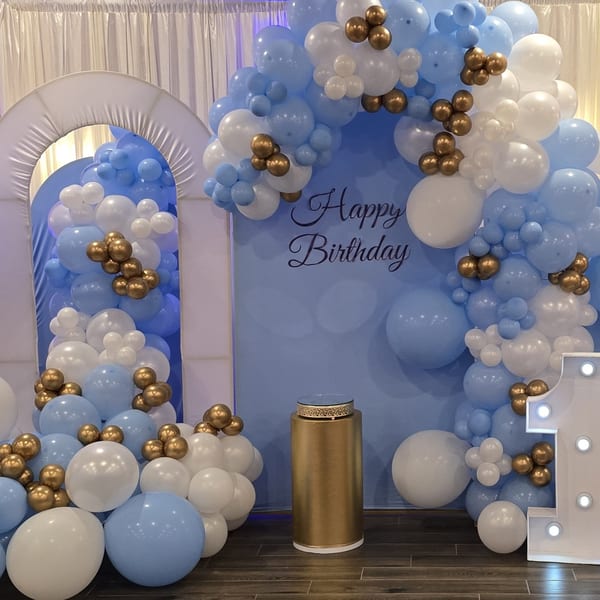 A birthday decoration with blue, white, and gold balloons, a "Happy Birthday" sign, and a golden pedestal.