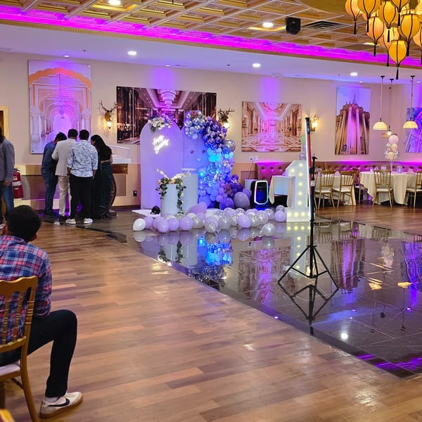 A large, ornate event hall with purple lighting, balloons, and Indian-themed decor.