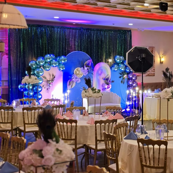 An Indian restaurant event space with round tables, gold chairs, and a blue and purple balloon arch.