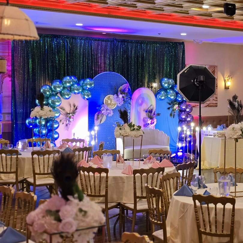 An Indian restaurant event space with round tables, gold chairs, and a blue and purple balloon arch.