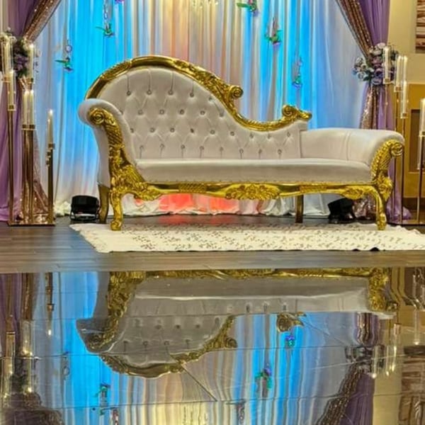 Ornate gold and white chaise lounge on a stage with purple and blue draped curtains.
