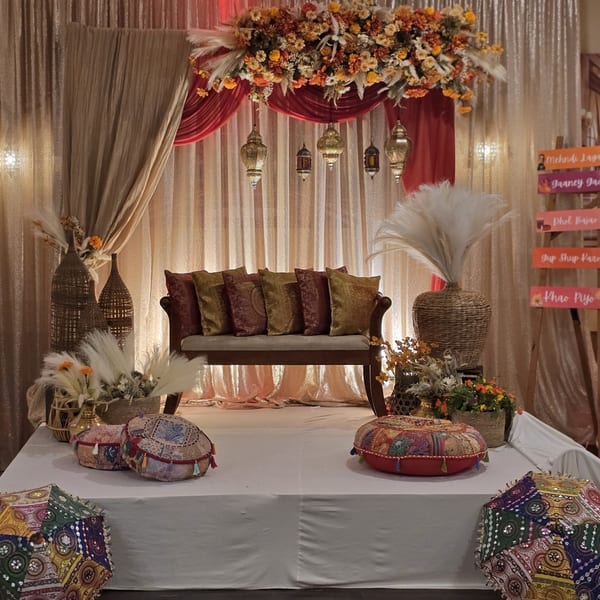 An Indian-themed stage with a sofa, colorful pillows, lanterns, and floral decorations against a gold curtain.