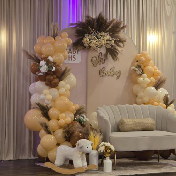 A baby shower setup with balloons, a plush rocking sheep, and a small sofa.