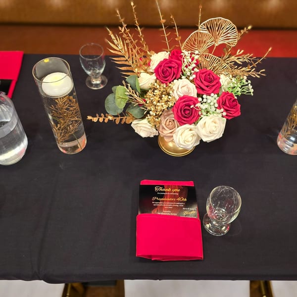 A black table set with a floral centerpiece, candles, glasses, and a red thank you card.