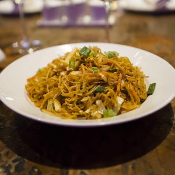 A white plate filled with golden noodles, vegetables, and chicken, garnished with green onions.