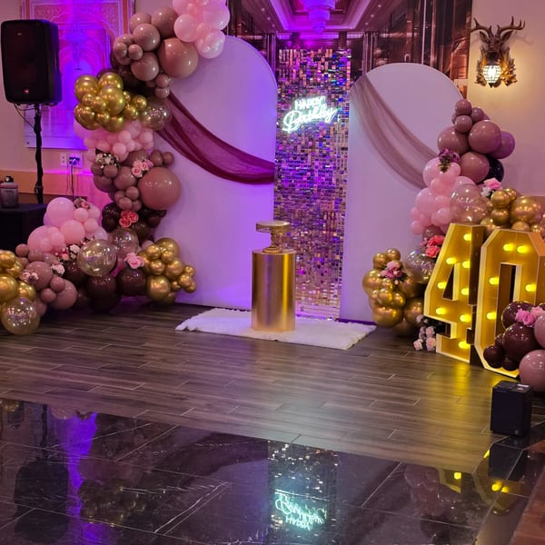 A birthday party setup with pink and gold balloons, a "Happy Birthday" neon sign, and light-up "40" numbers.