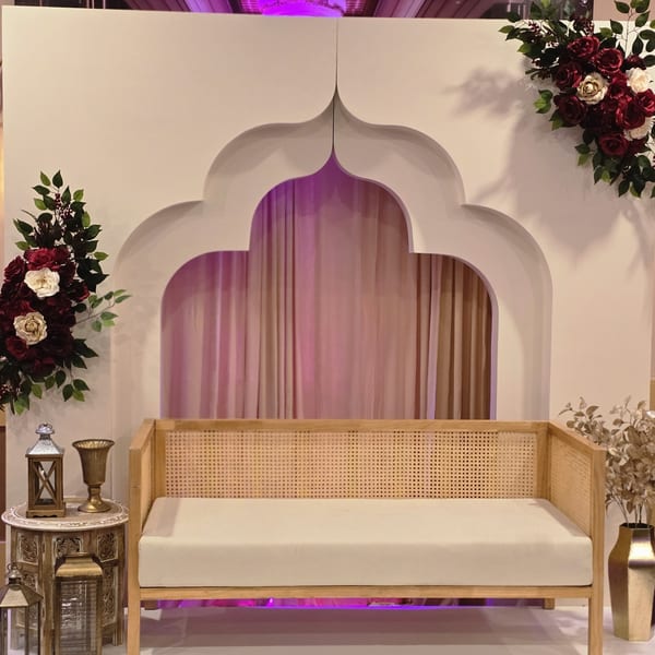 An Indian-inspired seating area with a wooden bench, decorative archway, and floral arrangements.