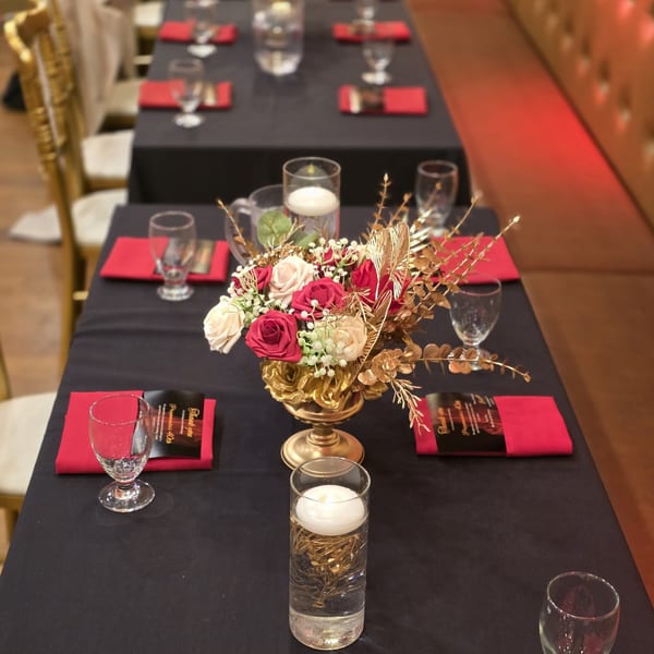 Elegant dining tables set with black tablecloths, red napkins, wine glasses, and floral centerpieces.