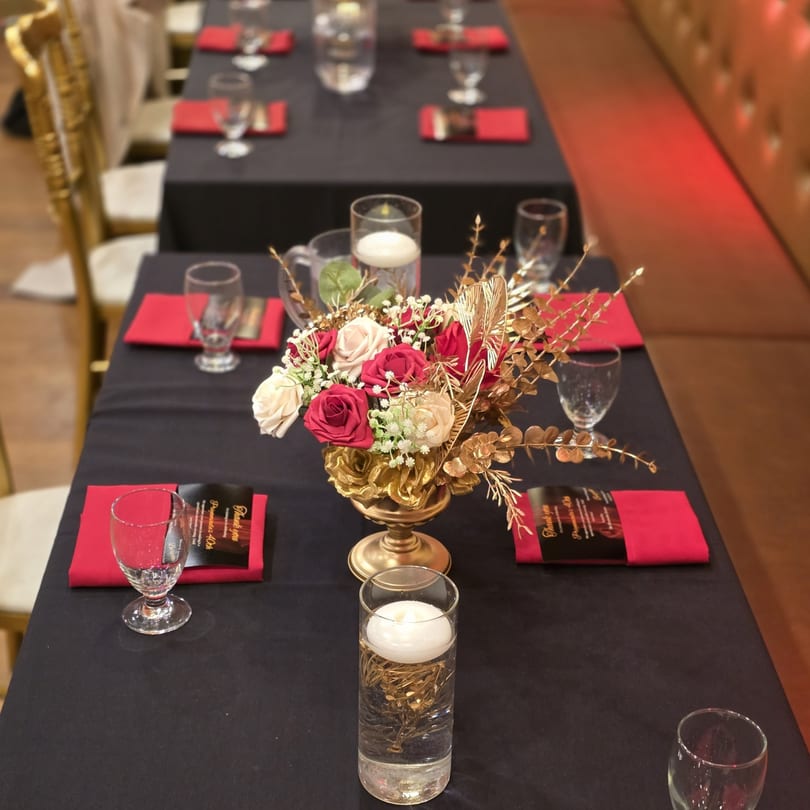 Elegant dining tables set with black tablecloths, red napkins, wine glasses, and floral centerpieces.