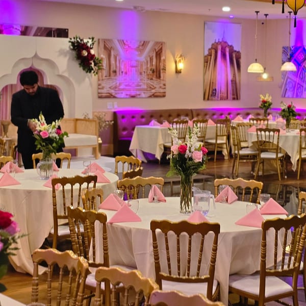 A man arranging flowers in a vibrant Indian restaurant dining room with pink lighting and elegant table settings.