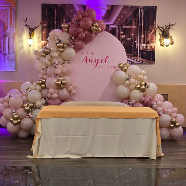 A baby shower setup with a pink backdrop, balloons, and a table with a yellow runner.