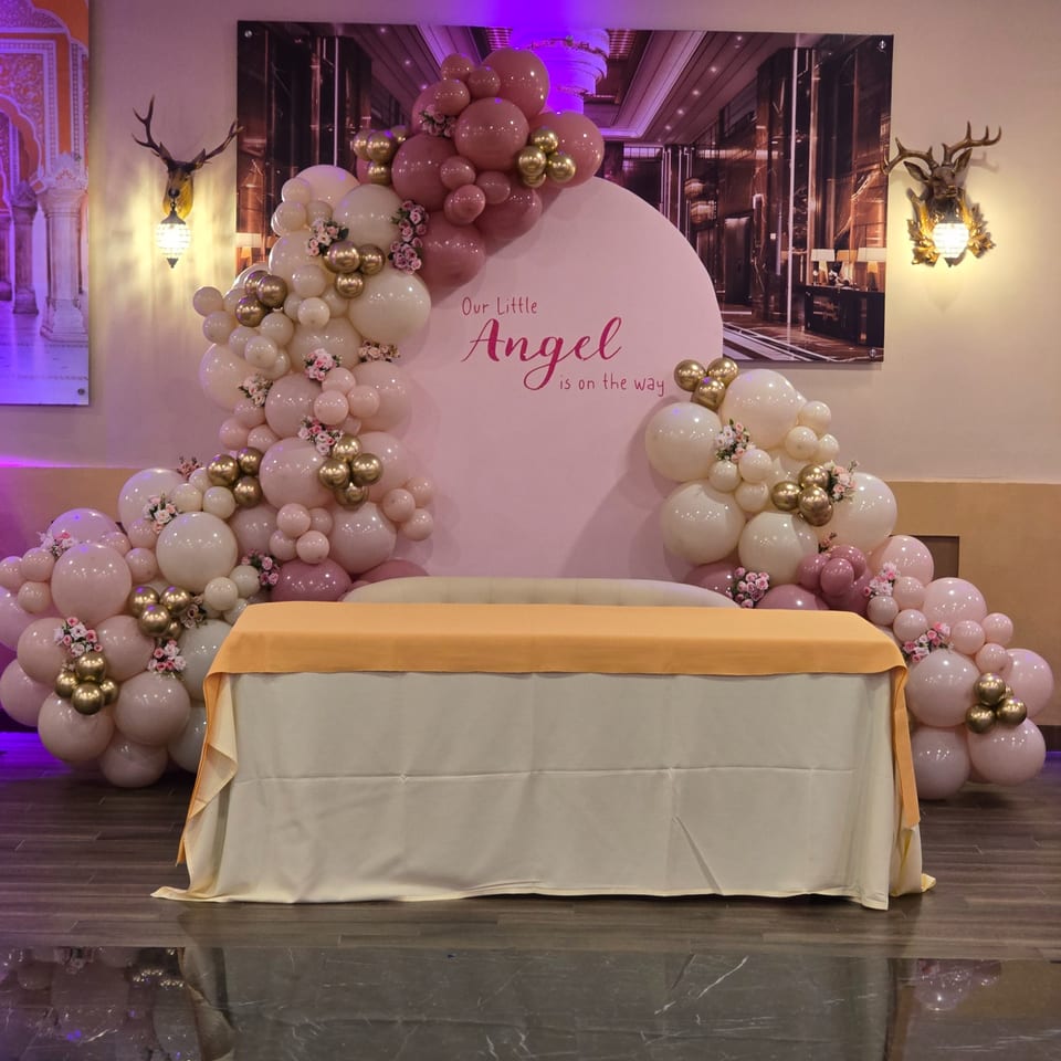 A baby shower setup with a pink backdrop, balloons, and a table with a yellow runner.