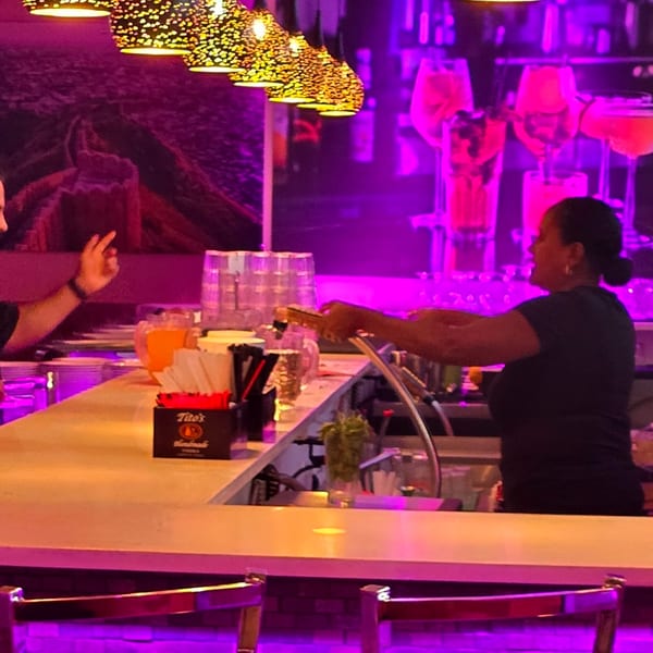 Bartender serving drinks at a vibrant bar with purple lighting and decorative hanging lamps at Spice Culture.
