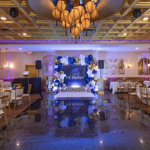 An Indian restaurant interior with a graduation balloon arch, tables, and a DJ booth.