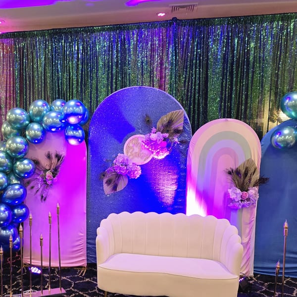 A vibrant party setup with a white sofa, blue and pink backdrops, balloons, and floral decor.