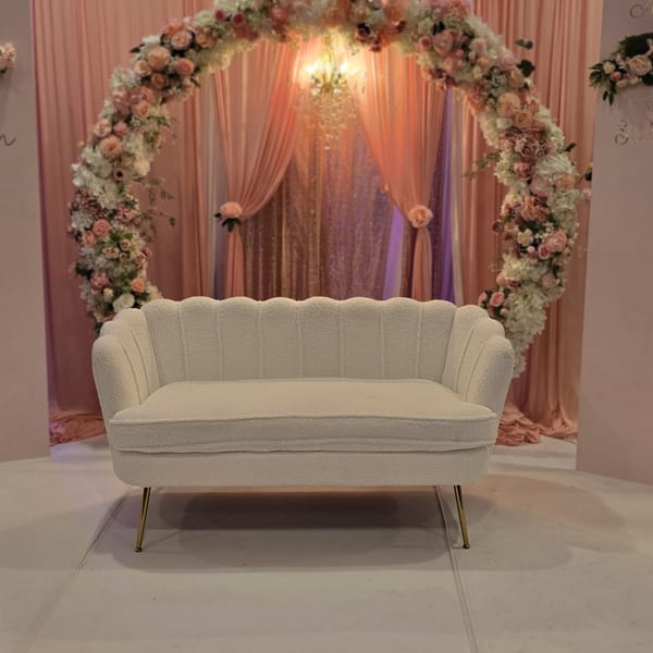 White scalloped sofa in front of a floral arch and pink draped curtains at Spice Culture.