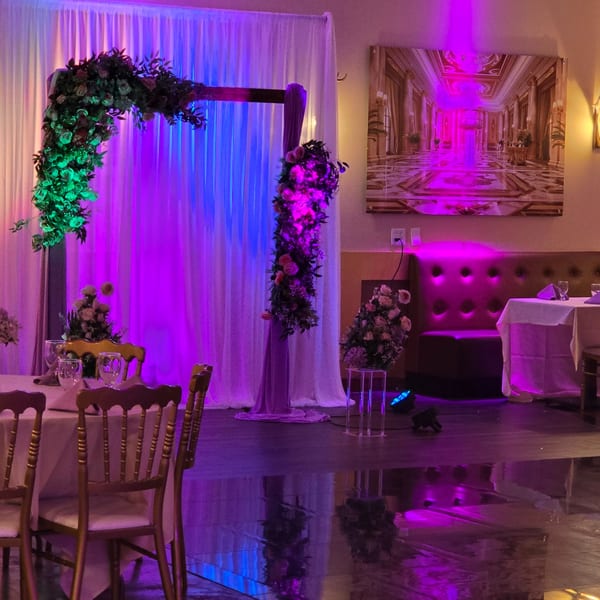 A restaurant dining area with purple and blue lighting, floral archway, and set tables.