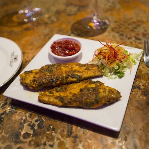 Two pieces of Indian spiced fish with a side of red chutney and a small salad.