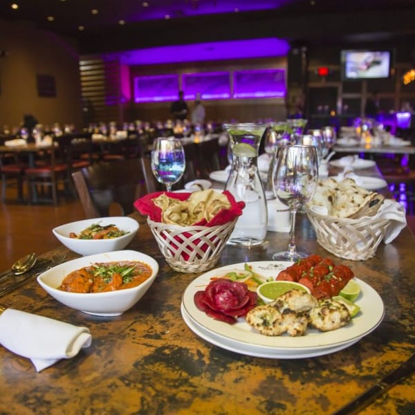 Indian dishes, including curries, naan, and grilled meats, on a table in a dimly lit restaurant.