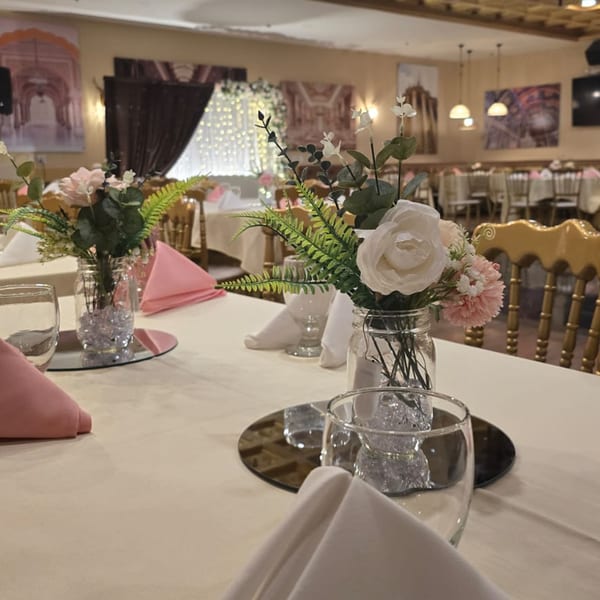 Elegant dining room at Spice Culture with tables set with floral centerpieces, pink napkins, and golden chairs.